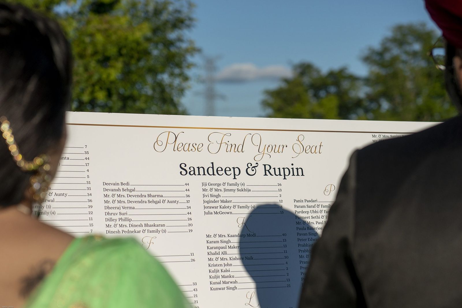 Guests reading a large printed seating chart outdoors at a wedding.