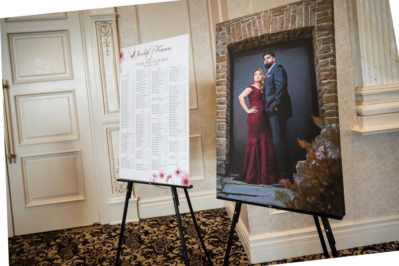 A printed seating chart on an easel at a ballroom entrance, guest names in columns beneath a script monogram.